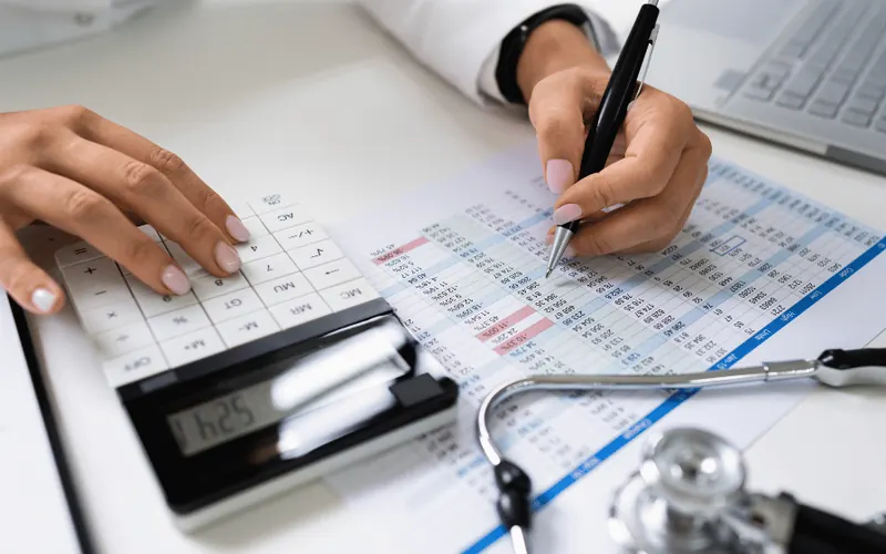 A hand marking up a coded medical chart beside a stethoscope and keyboard