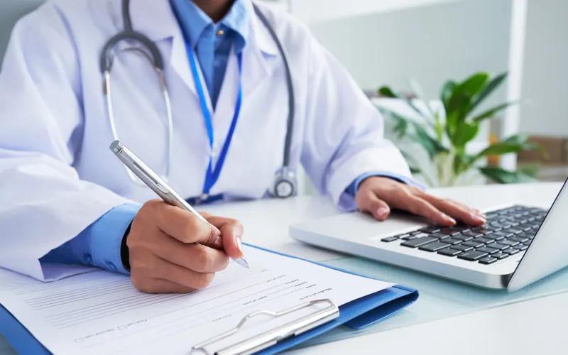 A clinician completing a documentation form beside an open laptop